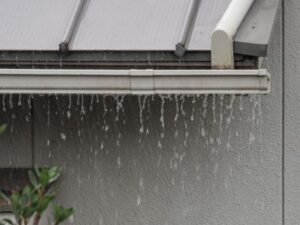雨樋から雨水があふれて外壁に向かって滴り落ちている様子