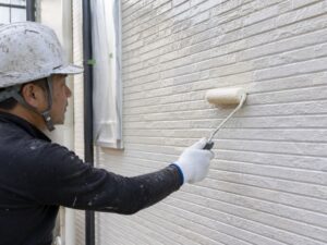 ヘルメット姿の職人がサイディングにクリヤー塗装を行う様子
